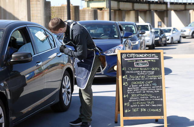 A volunteer takes an order for a bag of prepared sandwiches, from one of many that have waited in their cars for free food, in St. Louis on Sunday, April 26, 2020. Hundreds of cars lined the streets for an opportunity to receive food from several restaurants, while the group took donations for theThe Gateway Resilience Fund, an organization that assists fellow restaurant workers that are out of work because of the coronavirus.  SLP2020042604 BILLxGREENBLATT