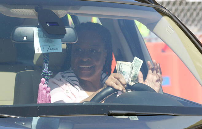 A woman waits for her order of prepared sandwiches, while a donation waits in her hand in St. Louis on Sunday, April 26, 2020. Hundreds of cars lined the streets for an opportunity to receive free food from several restaurants, while the group took donations for theThe Gateway Resilience Fund, an organization that assists fellow restaurant workers that are out of work because of the coronavirus.  SLP2020042605 BILLxGREENBLATT