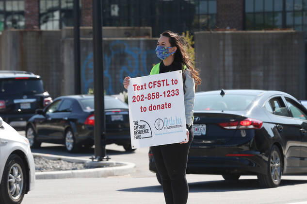 A volunteer holds a sign as hundreds line up in their cars to receive free food, in St. Louis on Sunday, April 26, 2020. Hundreds of cars lined the streets for an opportunity to receive food from several restaurants, while the group took donations for theThe Gateway Resilience Fund, an organization that assists fellow restaurant workers that are out of work because of the coronavirus.  SLP2020042608 BILLxGREENBLATT