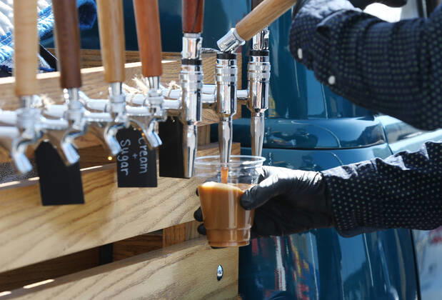 A volunteer draws a coffee for a person waiting in their car for free food, in St. Louis on Sunday, April 26, 2020. Hundreds of cars lined the streets for an opportunity to receive food from several restaurants, while the group took donations for theThe Gateway Resilience Fund, an organization that assists fellow restaurant workers that are out of work because of the coronavirus.  SLP2020042609 BILLxGREENBLATT