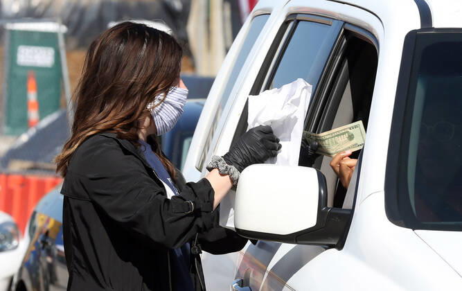 A volunteer hands off a bag of prepared sandwiches, to one of many that have waited in their cars for free food, in St. Louis on Sunday, April 26, 2020. Hundreds of cars lined the streets for an opportunity to receive food from several restaurants, while the group took donations for theThe Gateway Resilience Fund, an organization that assists fellow restaurant workers that are out of work because of the coronavirus.  SLP2020042610 BILLxGREENBLATT
