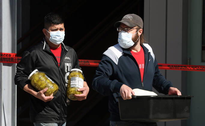 Volunteers carry food to be given away to the many that have waited in their cars for free food, in St. Louis on Sunday, April 26, 2020. Hundreds of cars lined the streets for an opportunity to receive food from several restaurants, while the group took donations for theThe Gateway Resilience Fund, an organization that assists fellow restaurant workers that are out of work because of the coronavirus.  SLP2020042613 BILLxGREENBLATT