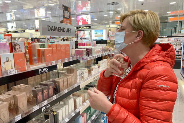 Lockerungen und Maskenpflicht in der Coronavirus Pandemie: Geschaefte in Bayern oeffnen am 27.April wieder. Eine Frau testet in einem Drogeriemarkt trotz Mund-Nasen-Schutz ein Parfum,Damenduft, Ladengeschaeft ,Filiale,Eingang,