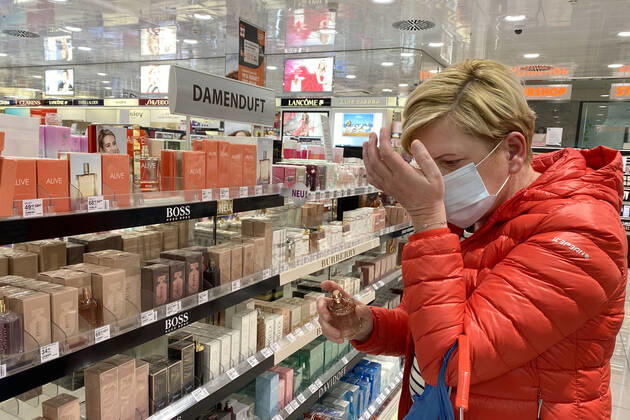 Lockerungen und Maskenpflicht in der Coronavirus Pandemie: Geschaefte in Bayern oeffnen am 27.April wieder. Eine Frau testet in einem Drogeriemarkt trotz Mund-Nasen-Schutz ein Parfum,Damenduft, Ladengeschaeft ,Filiale,Eingang,