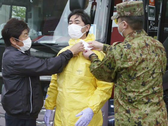 New coronavirus A Japan Ground Self-Defense Force member (R) shows a bus driver how to wear a protective suit at Narita airport, near Tokyo, on April 22, 2020, amid the coronavirus pandemic. Self-Defense Forces personnel are tasked with training bus drivers to transport people who arrived from overseas to hotels without being infected with the coronavirus. 