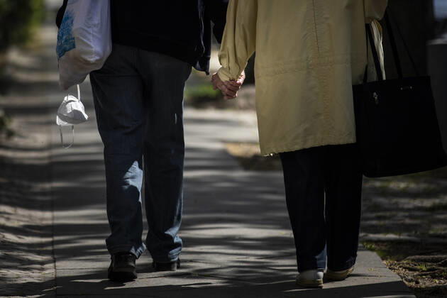 Ein aelteres Paar laeuft Hand in Hand, waehrend der Mann in der anderen Hand einen Mundschutz traegt, aufgenommen in Berlin, 28.04.2020. Deutschlandweit gibt es eine Maskenpflicht im Oeffentlichen Personennahverkehr. Berlin Deutschland