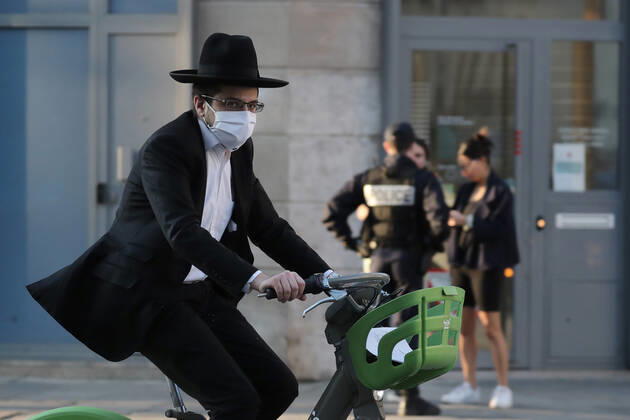A masked biker rides past security forces checking on residents permit to be in the streets of Paris, France, Tuesday April 28, 2020 as the country enters its 6th week of confinement. The French premier announced today that protective masks, which have been in severe shortage since the outbreak of the pandemic, will be available for everyone starting May 11th.  PAR20200428108 ECOxCLEMENT