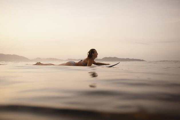 Female surfer lying on surfboard in the evening, Costa Rica model released Symbolfoto HWHF00010