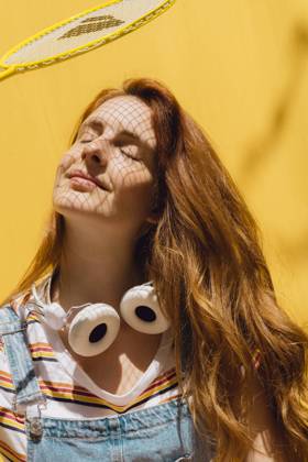 IMAGO Creative, Sommer, Schatten-Plätze bei Hitze Relaxed young woman with badminton racket over face wearing headphones around neck during sunny day model released Symbolfoto property released AFVF06451