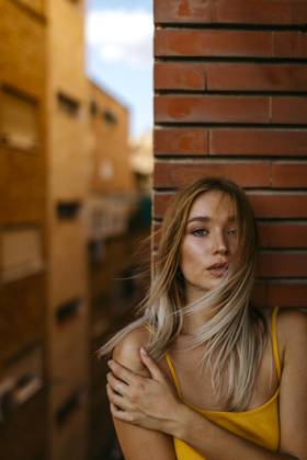 Beautiful woman with long blond hair standing against brick wall in balcony model released Symbolfoto TCEF00718