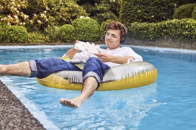 Young man working from home office on airbed in swimming pool looking at architectural model model released Symbolfoto property released UKOF00003