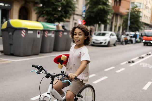 Creative Highlights Symbolfotos Carefree boy holding skateboard while riding bicycle on street model released Symbolfoto VABF03074