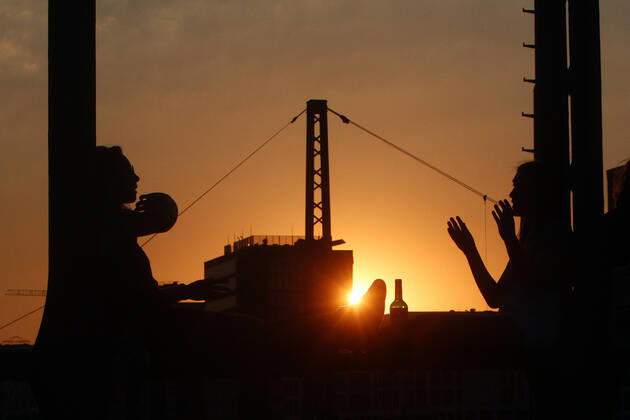 Ein Paar sitzt im Gegenlicht der untergehenden Sonne auf einem Träger der Hackerbrücke in München und unterhält sich, Bayern, Deutschland.