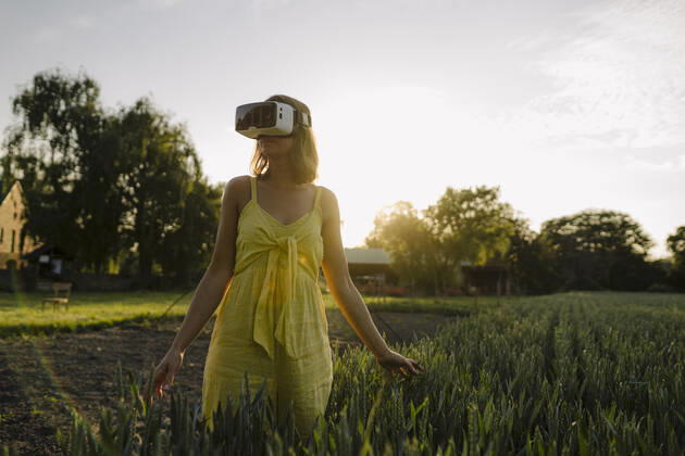 Young woman wearing VR goggles in a grain field in the countryside model released Symbolfoto property released GUSF04276