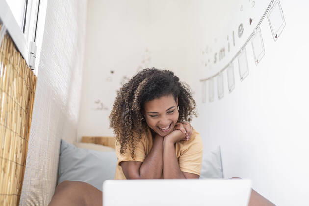 Creative Highlights Symbolbilder Cheerful woman with curly hair video conferencing over laptop while sitting by wall at home model released Symbolfoto property released SNF00529