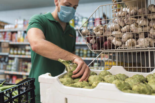 A shopkeeper with a mask taking artichokes from a box in the fruit shop. Torredelcampo, AL, Spain CR_NNSU200920A-508791-01 ,model released, Symbolfoto ,property released