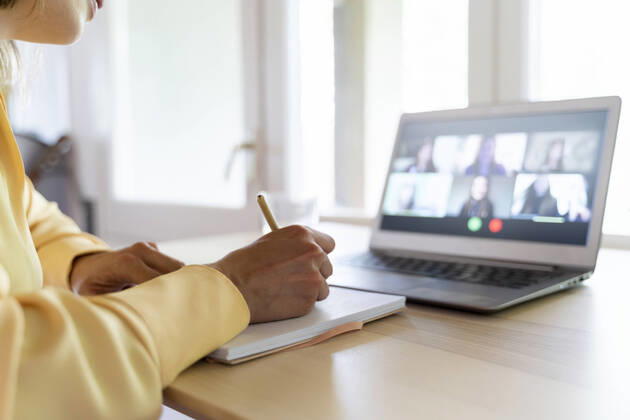 Cropped hands of female entrepreneur writing on diary while talking with colleagues through video conference at home model released Symbolfoto property released AFVF07054