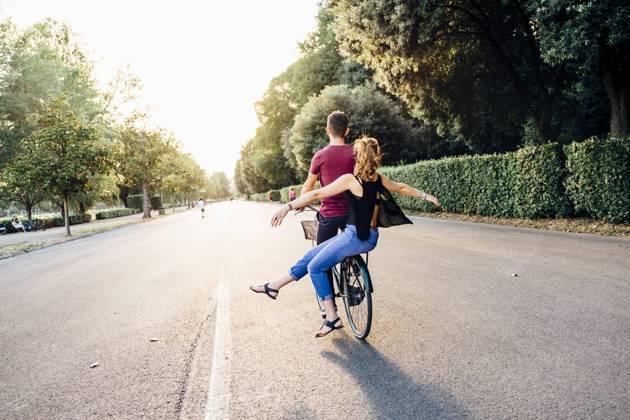 Young woman with arms outstretched sitting with boyfriend on bicycle in park model released Symbolfoto SBAF00032