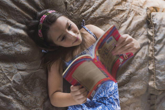 IMAGO Creative: Digitale Welt, Verzicht auf Technologie Smiling girl reading book while lying on bed at home model released Symbolfoto DSIF00137