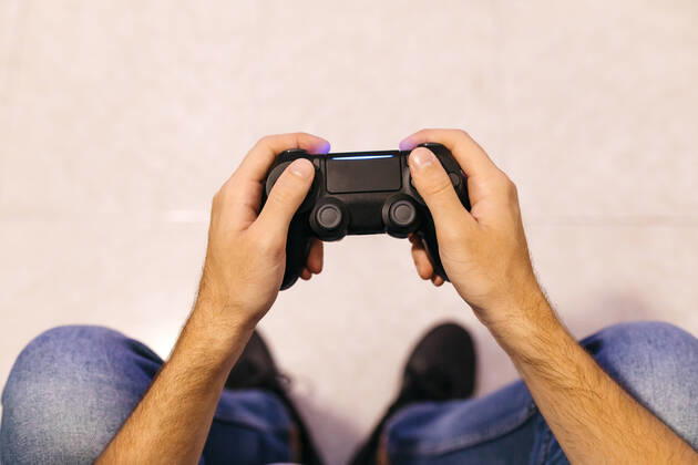 IMAGO Creative, Lifestyle, Gaming Young male gamer holding controller while playing at home model released Symbolfoto property released JRFF04749