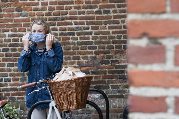 Young blond woman standing next to bicycle with basket, putting on face mask. United Kingdom,Young blond woman standing next to bicycle with basket, putting on face mask. Young blond woman standing next to bicycle with basket, putting on face mask.
