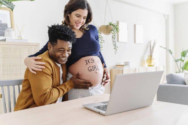 Husband and pregnant wife celebrating ultrasound results in front of a laptop, with a phrase written on her belly that it is a girl. Parenthood concept Sant Cugat del Vallès, CT, Spain CR_KTUU201128-569171-01 ,model released, Symbolfoto ,property released