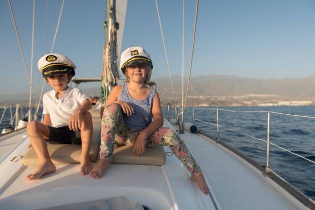 Positive kids in captain hats sitting on deck of expensive boat floating on water in sunny day, Model released, Property released Copyright: xAlvaroxHernandezx MR
