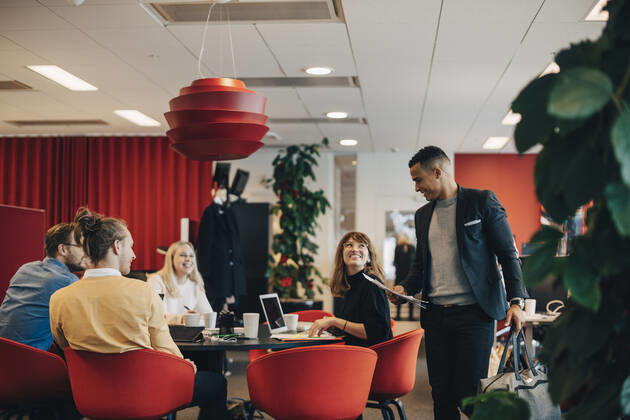 Smiling colleagues looking at businessman standing with bag and documents at office , model released, property released Copyright: xMaskotx , MA59842