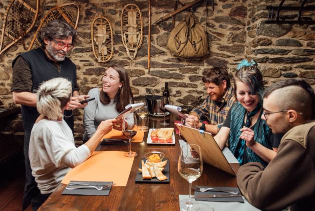 IMAGO Creative: Landleben - Essen Cheerful group of hipsters sitting at wooden table with menu and talking to waiter while ordering food during date in cafe, Model released, Property released Copyright: xGaldricxPenarrojax MR