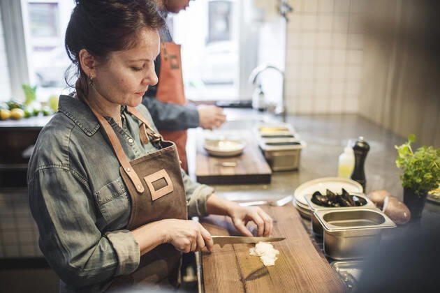 IMAGO Creative: Landleben - Essen Mature female chef cutting food on board at counter in restaurant kitchen , model released, property released Copyright: xMaskotx , MA61522