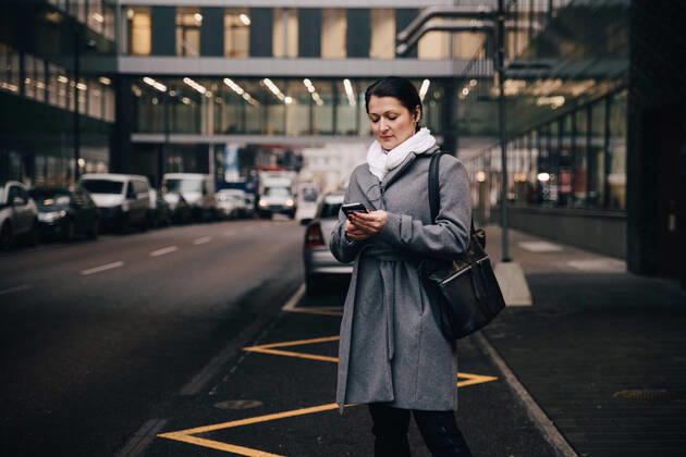 IMAGO Creative: Corporate: Klimaschutz, Digitalisierung und Urbanisierung Businesswoman using smart phone while standing on city street against building , model released Copyright: xMaskotx , MA69262