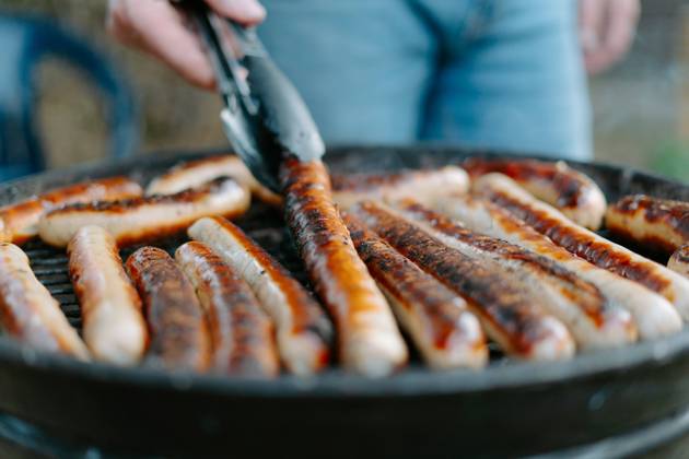 Crop anonymous person in jeans frying delicious beef sausages on grill and using tongs while having barbecue picnic on backyard Copyright: xJakexJakabx Model Released