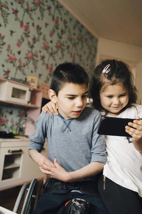 IMAGO Creative: Jahreszeit Winter, Fantasievoll drinnen spielen Sister showing video to autistic brother on smart phone at home , model released, property released Copyright: xMaskotx , MA72520