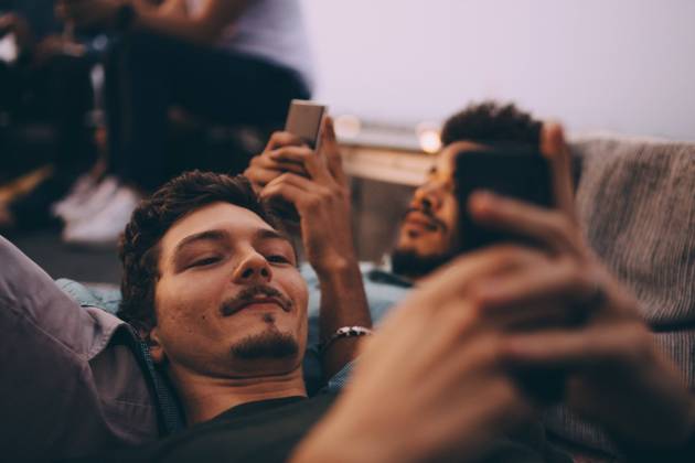 IMAGO Kreativ: Urbane Kultur - Sommer auf den Dächern Young male friends using smart phones while lying on terrace at dusk , model released, property released Copyright: xMaskotx , MA75543