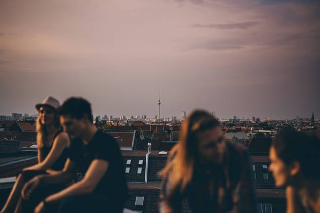 IMAGO Kreativ: Urbane Kultur - Sommer auf den Dächern Friends talking while sitting on terrace during rooftop party in city at dusk , model released, property released Copyright: xMaskotx , MA75664