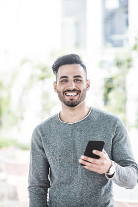 Portrait of smiling businessman holding mobile phone while standing in office , model released, property released Copyright: xMaskotx , MA77820