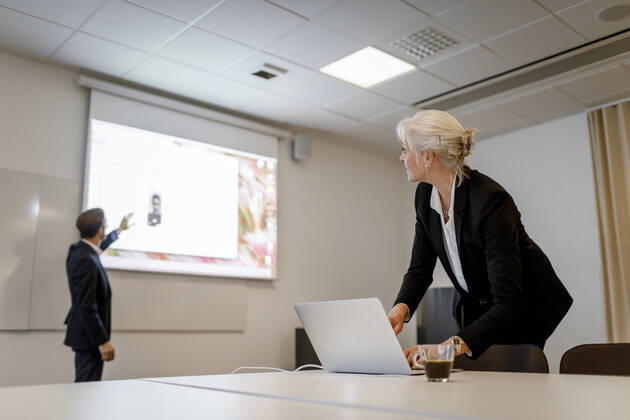 Female professional using laptop while male colleague standing by flat screen during video conference in board room at o Sweden, Stockholm, model released, property released Copyright: xMaskotx , MA79475