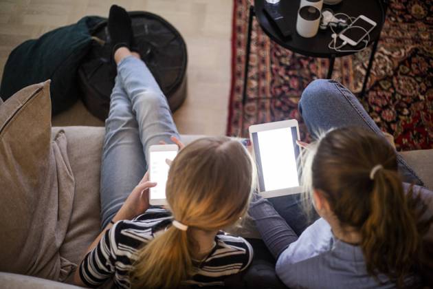 High angle view of sisters using wireless technologies while sitting on sofa at home Sweden, Stockholm, model released, property released Copyright: xMaskotx , MA80363