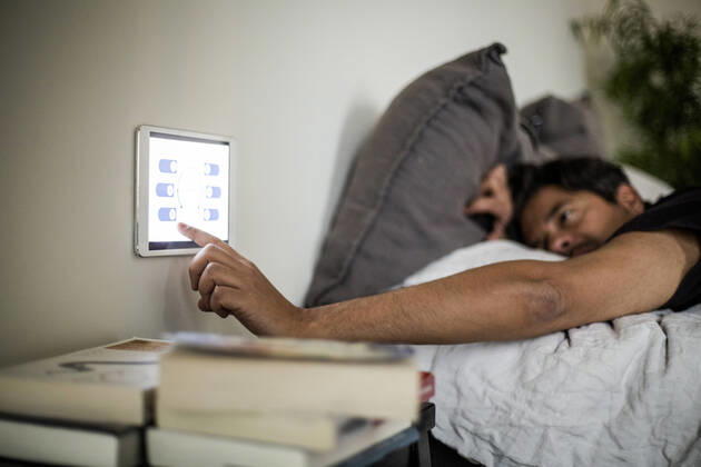 Man using digital tablet mounted on wall while lying on bed at smart home Sweden, Stockholm, model released, property released Copyright: xMaskotx , MA80376