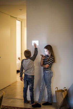 Brother using digital tablet mounted on wall while sister text messaging on mobile phone in smart home Sweden, Stockholm, model released, property released Copyright: xMaskotx , MA80402