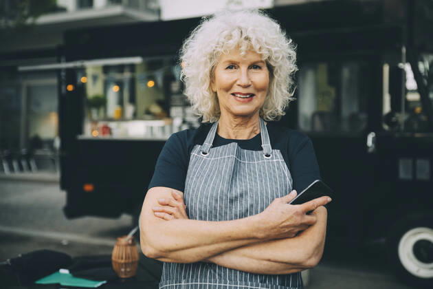 Portrait of senior owner with smart phone standing against food truck in city Sweden, Stockholm, model released, property released Copyright: xMaskotx , MA81560