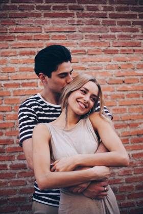 Young cheerful couple in casual clothes having fun during dating outdoors embracing in front of brick wall, Model released Copyright: xRamonxLopezx MR