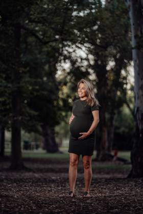 Happy pregnant woman in casual dress stroking belly while standing on pathway in park with green trees in sunny summer day with blue sky, Model released Copyright: xSantixMiquelx MR