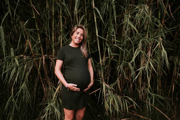 Happy pregnant woman in casual dress stroking belly while standing on green trees wall in sunny summer day with blue sky, Model released Copyright: xSantixMiquelx MR