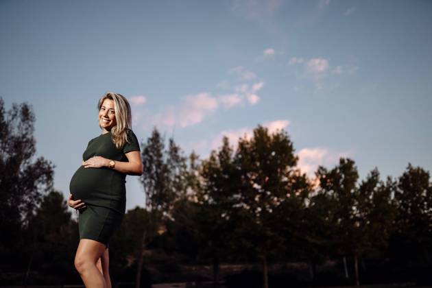Happy pregnant woman in casual dress stroking belly while standing on pathway in park with green trees in sunny summer day with blue sky, Model released Copyright: xSantixMiquelx MR