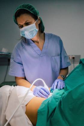 Female doctor in sterile mask and blue glove using ultrasound scanner while examining pregnant woman and looking at computer screen in hospital, Model released, Property released Copyright: xSixAndxSix MR