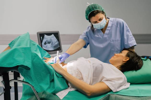 Female doctor in sterile mask and blue glove using ultrasound scanner while examining cheerful pregnant woman in hospital, Model released, Property released Copyright: xSixAndxSix MR