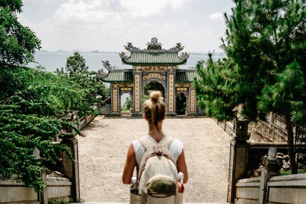 Back view of anonymous female tourist with backpack standing on stairs in front of arch of Buddhist temple in Vietnam Copyright: xVictorxGonzalezx Model Released