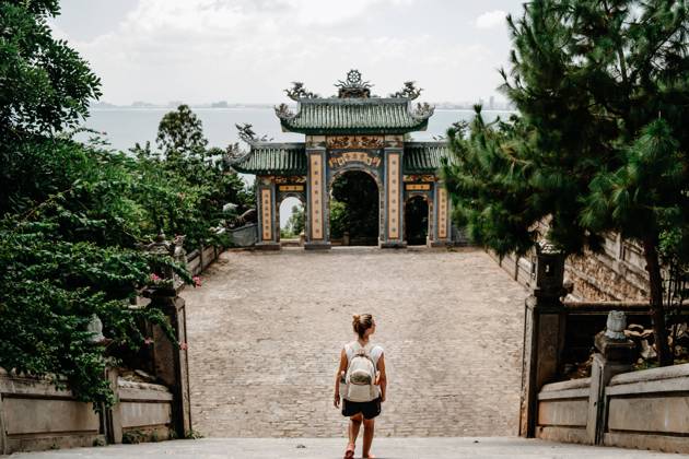 Back view of anonymous female tourist with backpack standing on stairs in front of arch of Buddhist temple in Vietnam Copyright: xVictorxGonzalezx Model Released