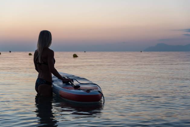 Side view of of unrecognizable female surfer standing near paddleboard and rowing against spectacular sun in sunset sky Copyright: xVictorxPrietox Model Released